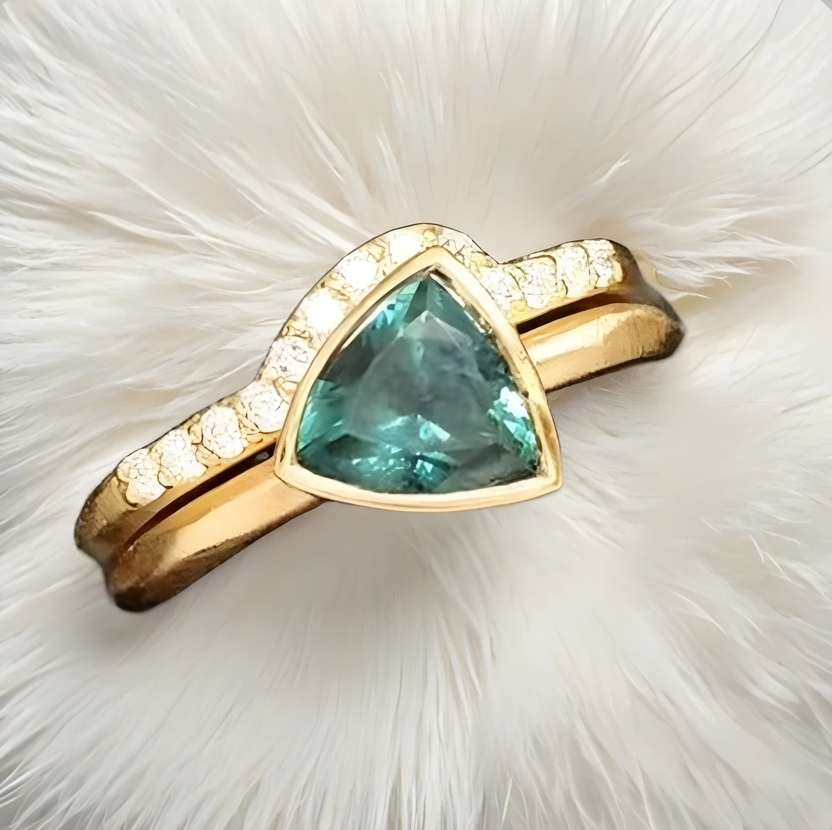 Gold ring with a green gemstone on a white fur background