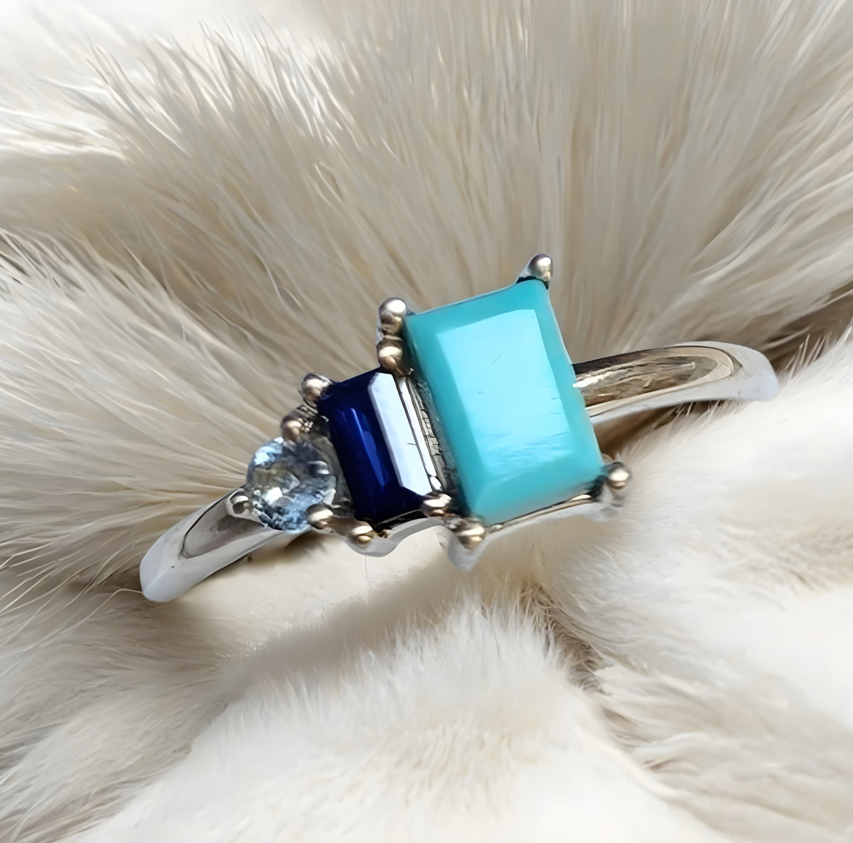 Silver ring with blue and green gemstones on a white fur background