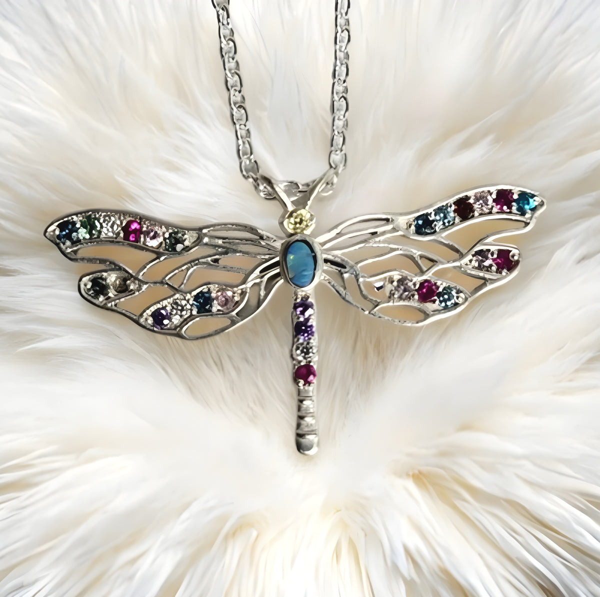 Dragonfly-shaped necklace with gemstones on a fluffy white surface